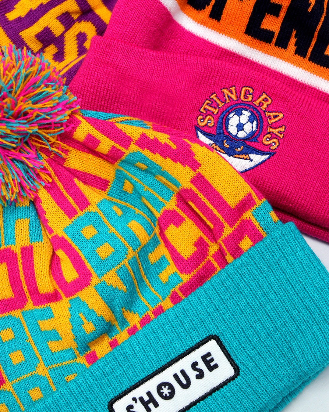 a close up of a colourful pom pom beanie that is pink, blue and yellow